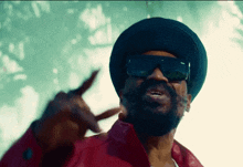a man wearing sunglasses and a hat is pointing at the camera