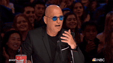 a bald man sitting in front of a crowd with a sonic drink in front of him