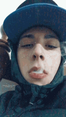 a young man wearing a blue hat and a black jacket is smoking a cigarette