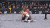 a wrestler is kneeling down in a wrestling ring while another wrestler is standing up .