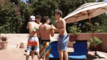 a group of young men are standing around a pool with a white umbrella