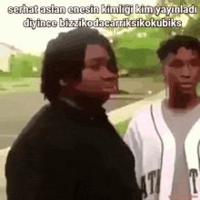 a man in a black shirt is standing next to another man in a white shirt with the word t on it
