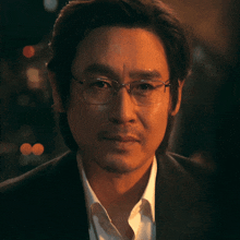 a man wearing glasses and a white shirt looks at the camera