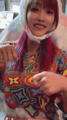 a girl with pink hair is wearing a colorful shirt and a hat .