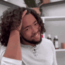 a man with curly hair and a beard is smiling while touching his head .