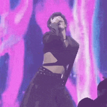 a man is covering his eyes while dancing on a stage in front of a purple background .