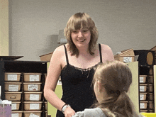 a woman in a black tank top smiles while talking to a girl
