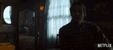 a man in a plaid shirt is sitting in a dark room with okay written on the bottom