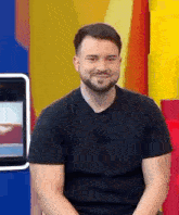 a man with a beard wearing a black shirt is sitting in front of a colorful wall .