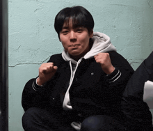 a man wearing a black jacket and a white hoodie has his fist up in the air