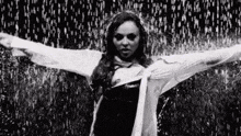 a woman in a white shirt is standing in the rain with her arms outstretched in a black and white photo .