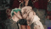 a man with green hair is kissing another man in a room .