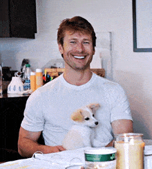 a man sitting at a table with a puppy on his lap and a bottle of aquafina water in the background