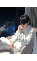 a man in a white suit sits in a chair with his hand on his face