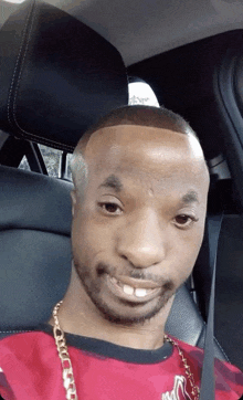 a man wearing a red shirt and a gold chain is sitting in the back seat of a car