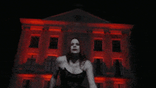 a woman in a black dress is standing in front of a building with red lights on it