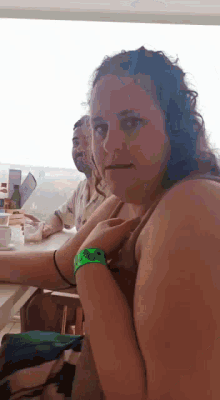 a woman is sitting at a table with a green wristband that says ' disney ' on it .