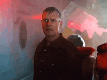 a man in a black shirt is standing in a dark room with red lights behind him