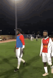 two soccer players are walking on a field with one wearing a red and white jersey with the letter r on it