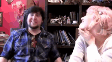 a man with a beard and a woman with pink hair are sitting in front of a bookshelf