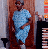 a woman in a blue hospital gown is dancing in front of a door with a sign that says elder on it