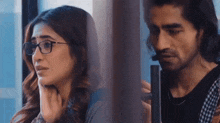a man and a woman are looking out of a window . the woman is wearing glasses .