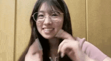 a woman wearing glasses and a pink shirt is smiling and holding her hair .