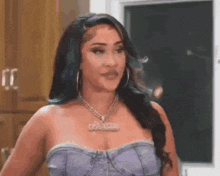 a woman wearing a purple top and a necklace is standing in front of a door .