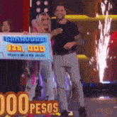 a man and a woman are standing next to each other on a stage holding a sign that says $ 25,000 pesos .