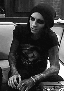 a black and white photo of a man sitting on a couch wearing a beanie .