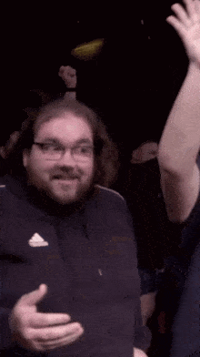 a man wearing glasses and a black adidas shirt holds up his fist