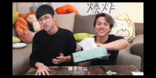 two men are sitting on a couch holding tissues .