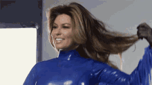 a woman in a blue latex suit is smiling and holding her hair