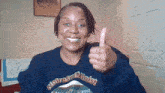 a woman wearing a noire feminist sweatshirt gives a thumbs up sign