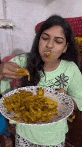 a woman in a green shirt is holding a plate of food and eating it