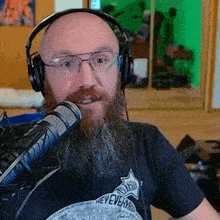 a bald man with a beard and glasses is wearing headphones and a black shirt .