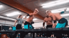 two men are wrestling in a ring with a referee in the background