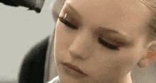 a close up of a woman 's face with her eyes closed and a hair dryer blow drying her hair .