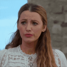 a woman wearing a white lace top looks sad