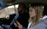 a man and a woman are sitting in a car and the woman is looking at her cell phone