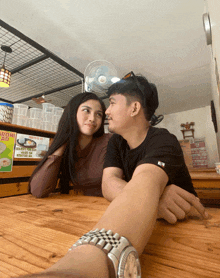 a man and a woman are sitting at a table in front of a sign that says " aroni tau "