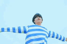 a man in a blue and white striped shirt with his arms outstretched against a blue sky