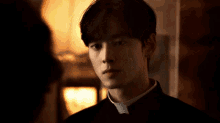 a young man in a priest 's uniform is standing in a dark room .