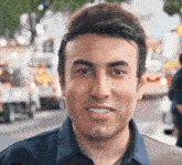 a man in a blue shirt is smiling in front of a blurry background