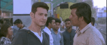 two men are standing next to each other and talking in a crowded street .