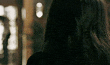 a woman with long dark hair is standing in front of a mirror looking at herself .