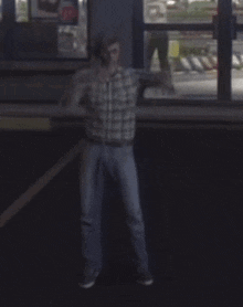 a man in a plaid shirt and jeans stands in a dark room