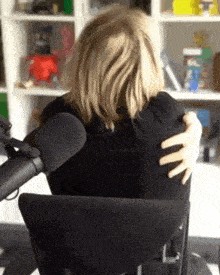 a woman is sitting in a chair with her hands on her shoulders in front of a microphone .