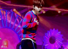 a man in a plaid sweater is dancing on a stage with purple lights .