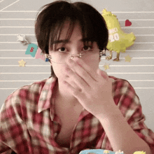 a man wearing glasses and a plaid shirt covering his face